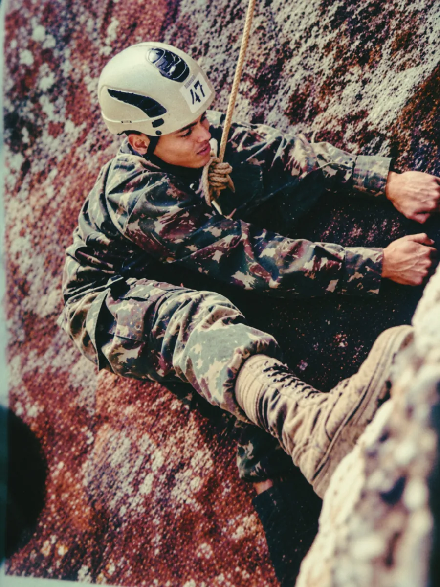 Guilherme Carvalho de Andrade escalando uma parede de rocha com capacete e corda, em treinamento de montanha do Exército Brasileiro.